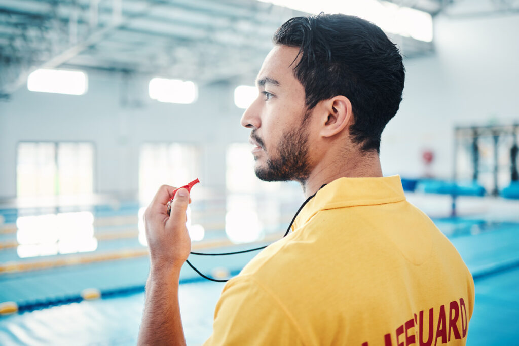 A lifeguard with a whistle beside a swimming pool